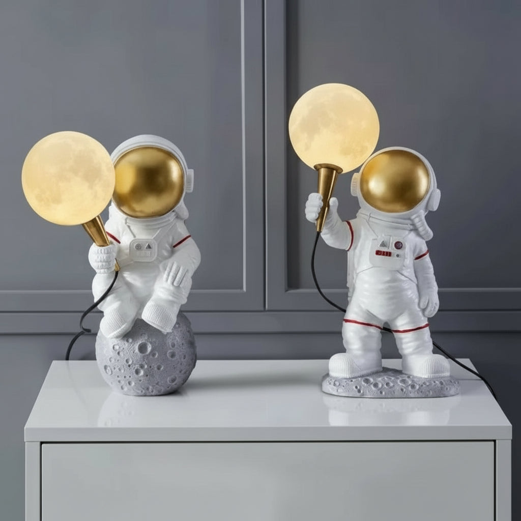 Two astronaut-themed table lamps with gold and moon-like designs on a gray surface.