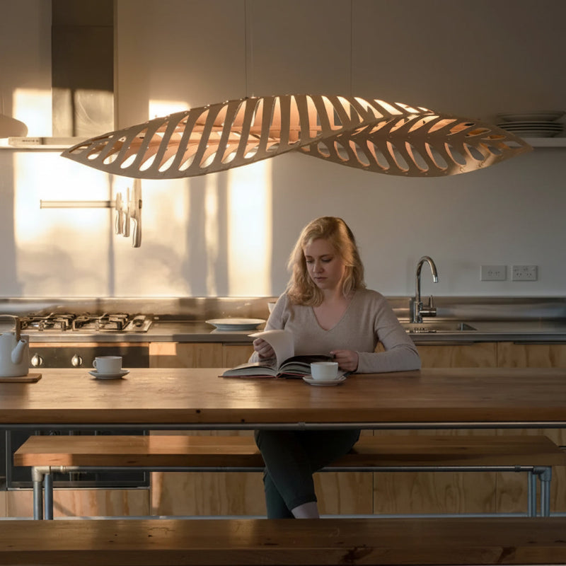Woman reading a book at a kitchen table with a modern pendant light above.
